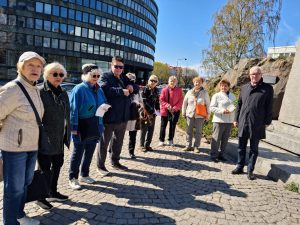 Ryhmä ihmisiä kokoontuneena kukkien laskemiseen muistomerkille.